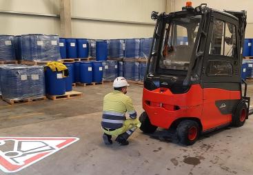 A man in a factory crouching down in front of a forklift
