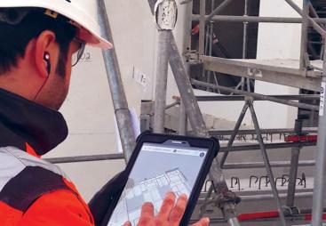 A man in orange PPE looking at a tablet screen