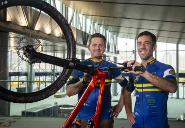 Two men in blue cycling clothes standing next to an upturned red bike and black wheel