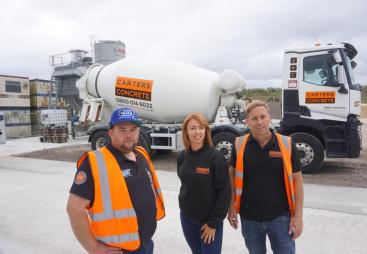 Two men and a woman in PPE in front of a concrete mixer