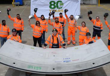 A group of people in orange PPE waving while standing next to a precast concrete tunnel segment