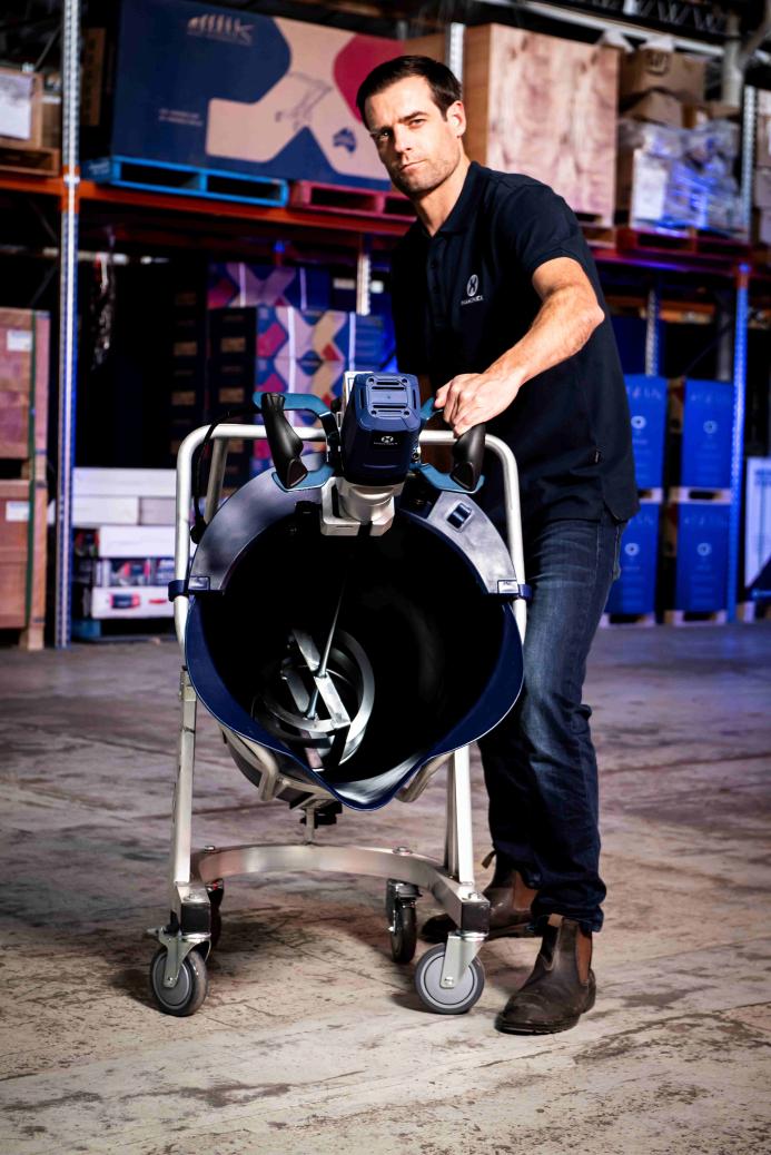A man in jeans and black shirt stands next to a portable screed mixer