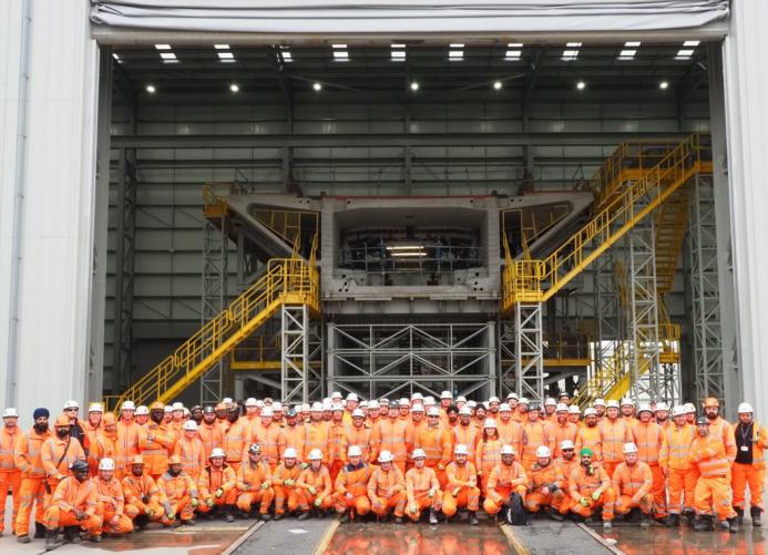 A group of people orange PPE standing in front of a precast concrete bridge pier