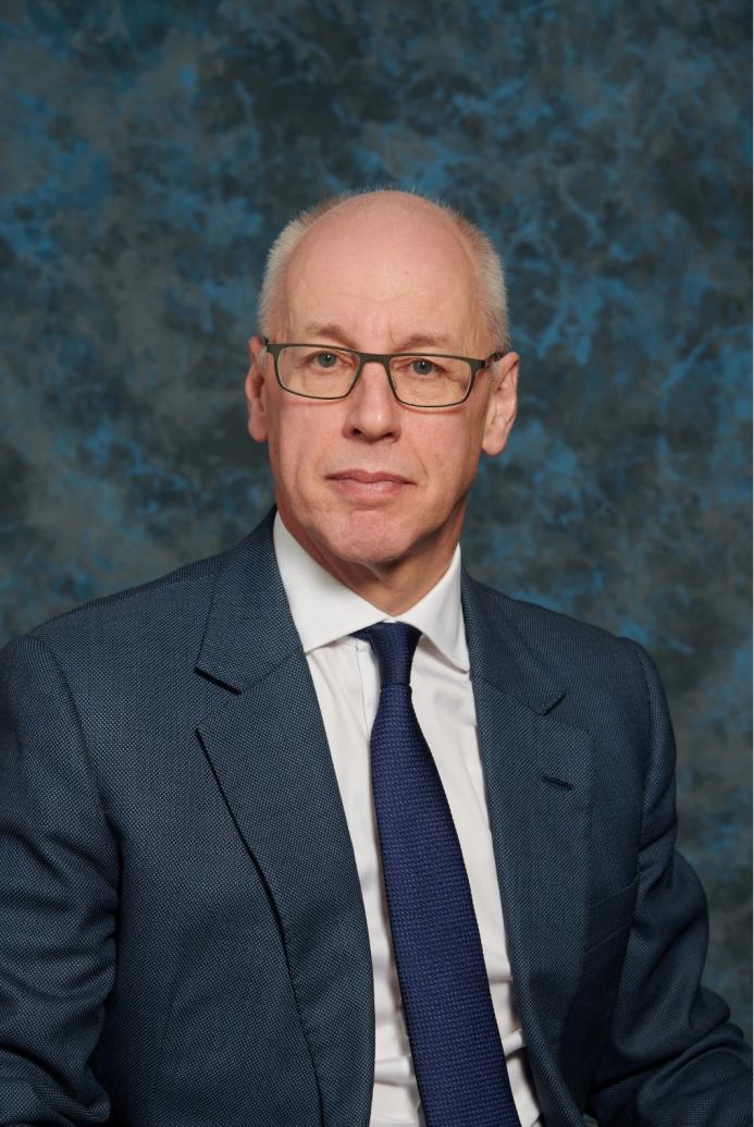 A studio head and shoulders photo of a man wearing glasses and a blue suit and tie