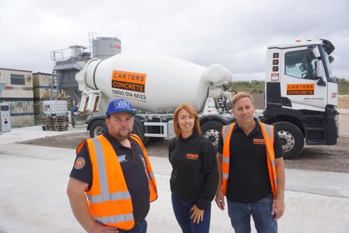 Two men and a woman in PPE in front of a concrete mixer