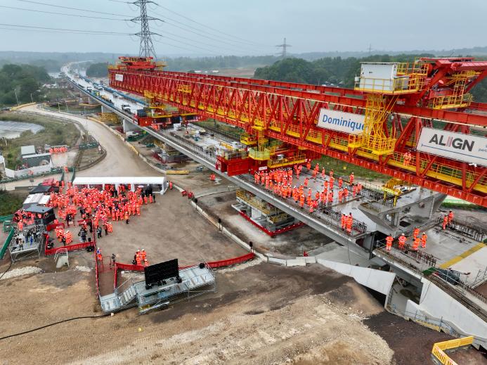 Two large groups of people in orange PPE standing on an under construction bridge deck