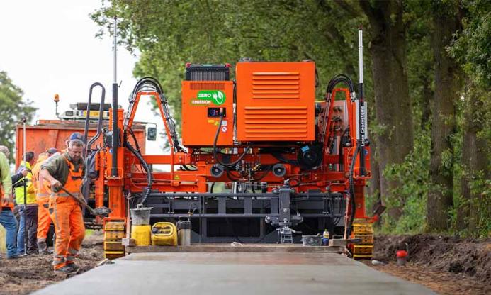 Men in orange PPE working on a raod paving project with an electric slipform paver