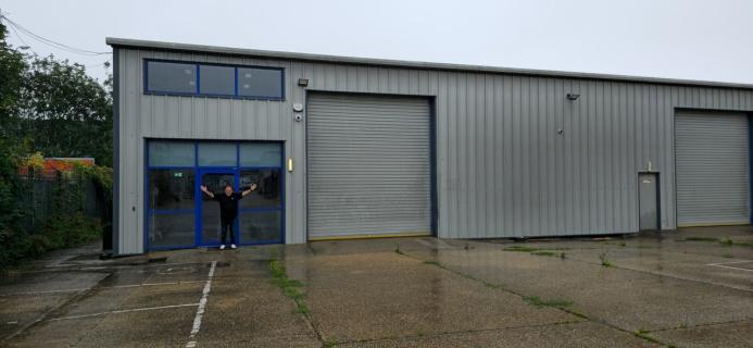 A bald man dressed in black outside a non-descript industrial estate