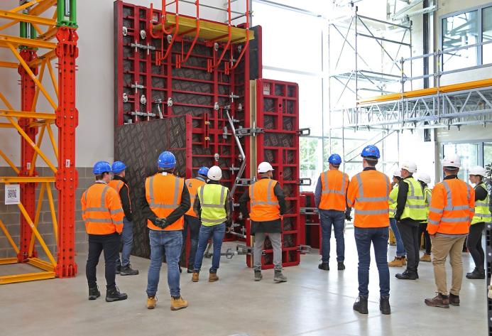 A group of people in orange PPE standing in front of red formwork panels