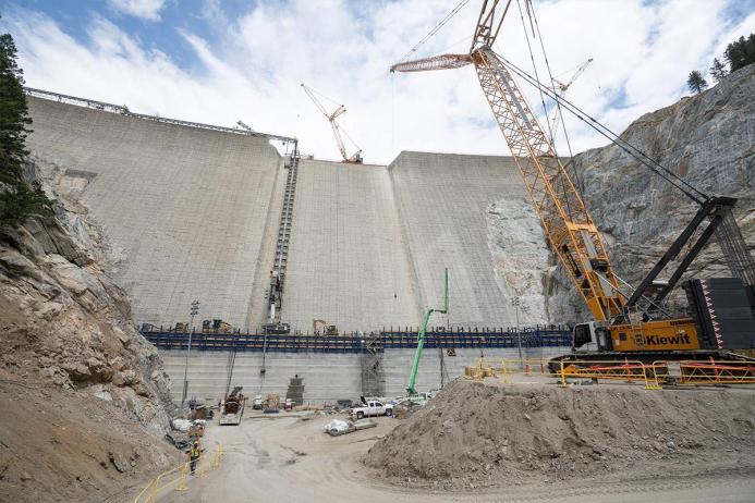 A yellow Liebherr crawler crane in front of a concrete RCC dam under construction