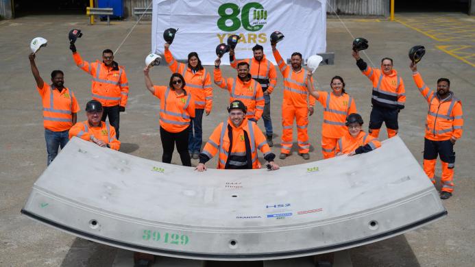 A group of people in orange PPE waving while standing next to a precast concrete tunnel segment