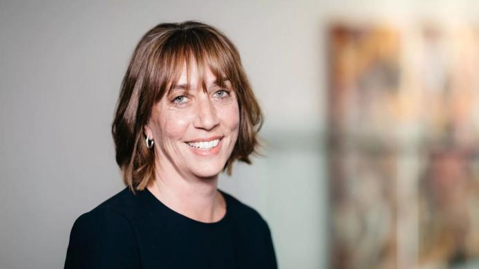 A head and shoulders photo of a smiling woman in black with reddish hair