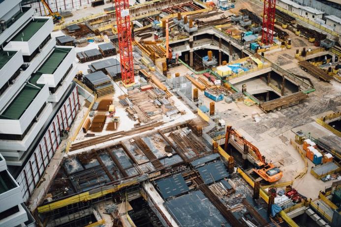 A construction site from above with a red tower crane and yellow excavators