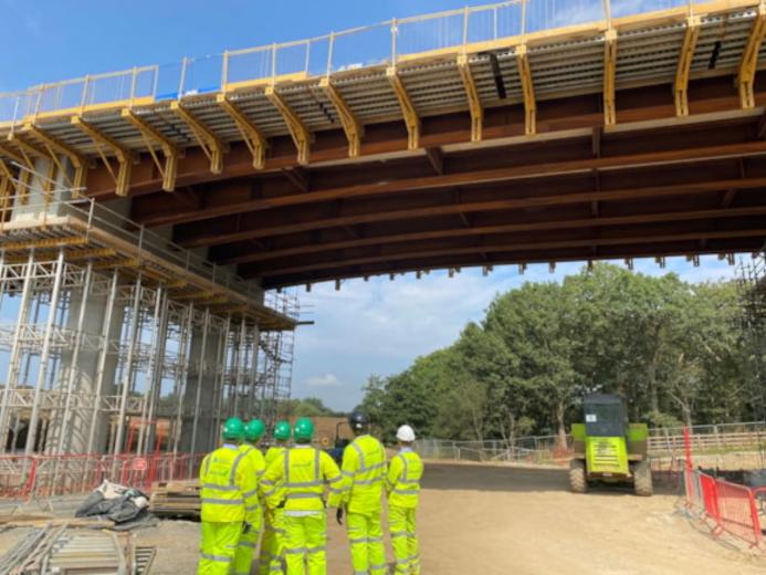 People in yellow PPE look at an under construction bridge
