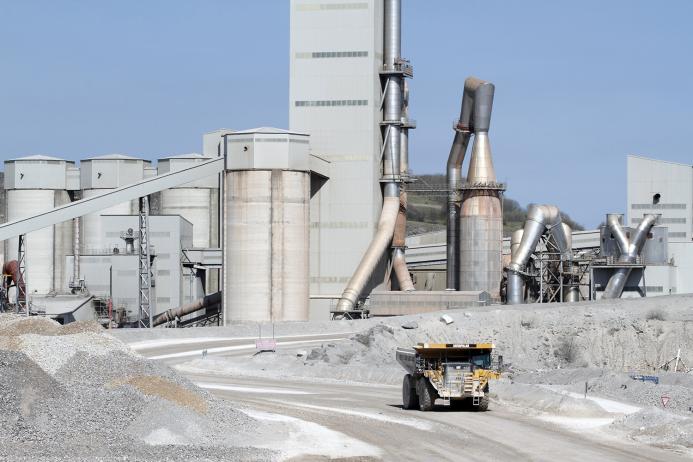 A yellow Caterpiller rigid dump truck (RDT) drives away from a huge cement factory 