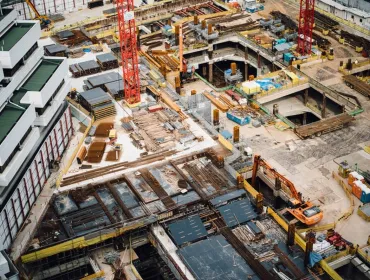 A construction site from above with a red tower crane and yellow excavators