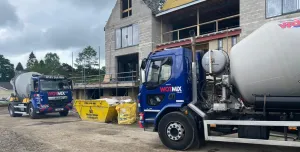 Two blue and grey concrete mixer trucks outside a new build house