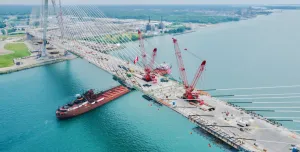 Aerial view of a bridge under construction across a river with two red cranes on its deck