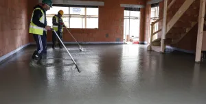 Two men in yellow PPE using screeds to level and internal concrete floor