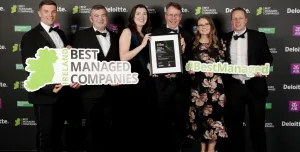 A group of men and women in evening wear at an awards ceremony holding a map of Ireland, a certificate and some cut-out words