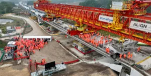 Two large groups of people in orange PPE standing on an under construction bridge deck