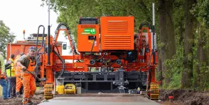 Men in orange PPE working on a raod paving project with an electric slipform paver