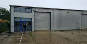 A bald man dressed in black outside a non-descript industrial estate