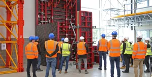 A group of people in orange PPE standing in front of red formwork panels