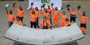 A group of people in orange PPE waving while standing next to a precast concrete tunnel segment