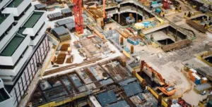 A costruction site with several peices of equipment including a red tower crane and a yellow excavator