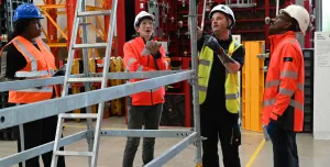 Three men in orange PPE and one in yellow inspect scaffolding