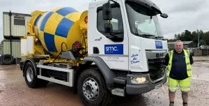 A man in yellow PPE stands in front of a white truck fitted with a yellow and blue concrete mixer