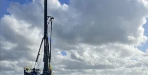 A Junttan piling rig stands in front of hundreds of pile caps, with a blue sky and dramatic clouds