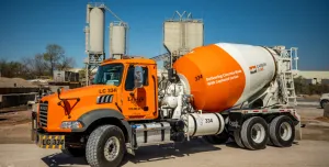 A bright orange concrete mixer truck at a cement plant