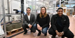 Three people crouch in front of the UK's first 3-D concrete printer