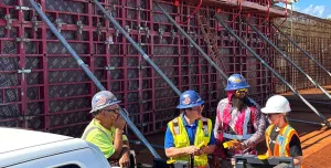 A group of construction workers in various colours of PPE stand in front of a wall of formwork