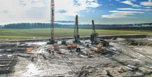 A large open area of country side with a crane and two piling rigs during construction of a circular tank that will be used to store radioactive waste in Slovenia.