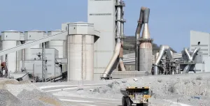 A yellow Caterpiller rigid dump truck (RDT) drives away from a huge cement factory 