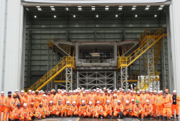 A group of people orange PPE standing in front of a precast concrete bridge pier
