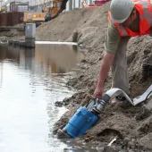 A man in red PPE holds a dewatering pump in water