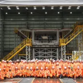 A group of people orange PPE standing in front of a precast concrete bridge pier