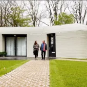 Two people walking down the garden path from a single story house