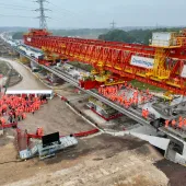 Two large groups of people in orange PPE standing on an under construction bridge deck