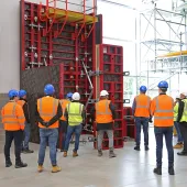 A group of people in orange PPE standing in front of red formwork panels