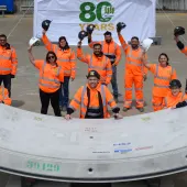 A group of people in orange PPE waving while standing next to a precast concrete tunnel segment