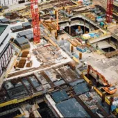 A costruction site with several peices of equipment including a red tower crane and a yellow excavator