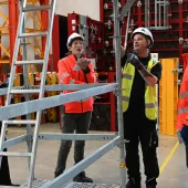 Three men in orange PPE and one in yellow inspect scaffolding