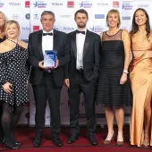 A group of people in evening wear in a line, on a stage accepting an award