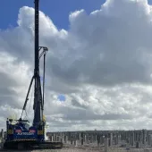 A Junttan piling rig stands in front of hundreds of pile caps, with a blue sky and dramatic clouds