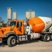 A bright orange concrete mixer truck at a cement plant